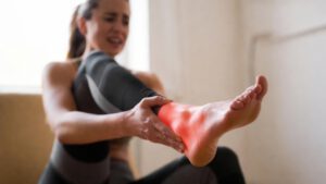 Sportlerin hält schmerzenden Fuß und Sprunggelenk – Symptom einer Sehnenscheidenentzündung im Fuß