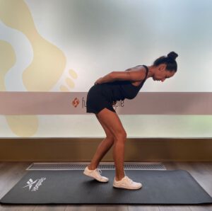 Frau in Sportkleidung befindet sich in der Endposition der Hip Hinge-Übung auf einer Trainingsmatte.