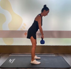 Frau führt die Bewegung des Kreuzhebens mit einer Kettlebell auf einer Trainingsmatte aus.